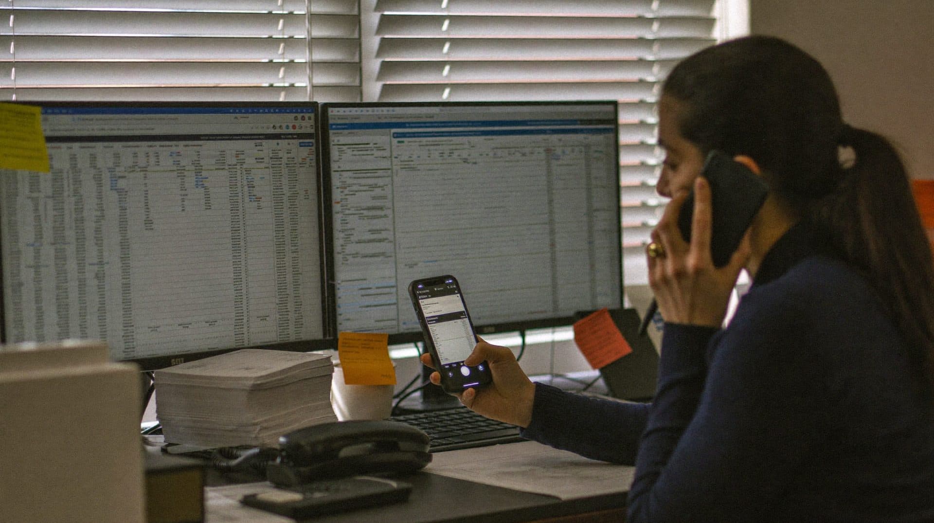 Operasyon ofisinde bir elinde telefon, diğerinde WhatsApp açık ikinci telefonla iki ekran arasında çalışan operasyon sorumlusu